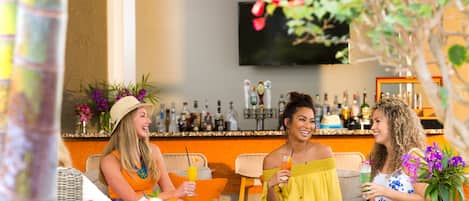 Een bar met rieten meubilair, een aan de muur bevestigde televisie en diverse flessen op planken.