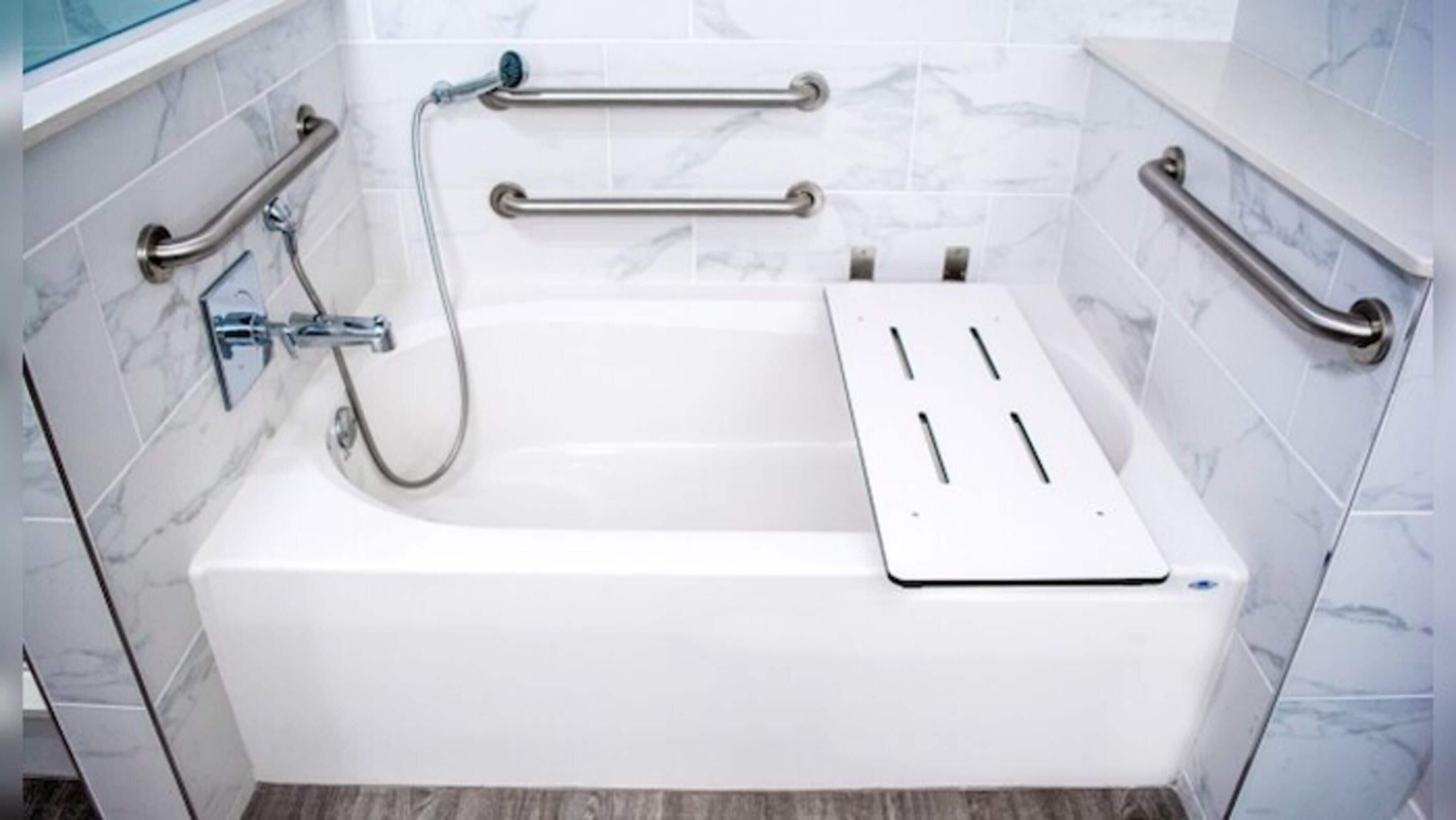 Un baño moderno con una bañera blanca, barras de apoyo y un cabezal de ducha manual.