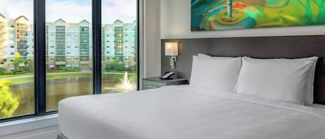 A hotel room with a large bed, a view of a water body, and a colorful abstract painting on the wall.