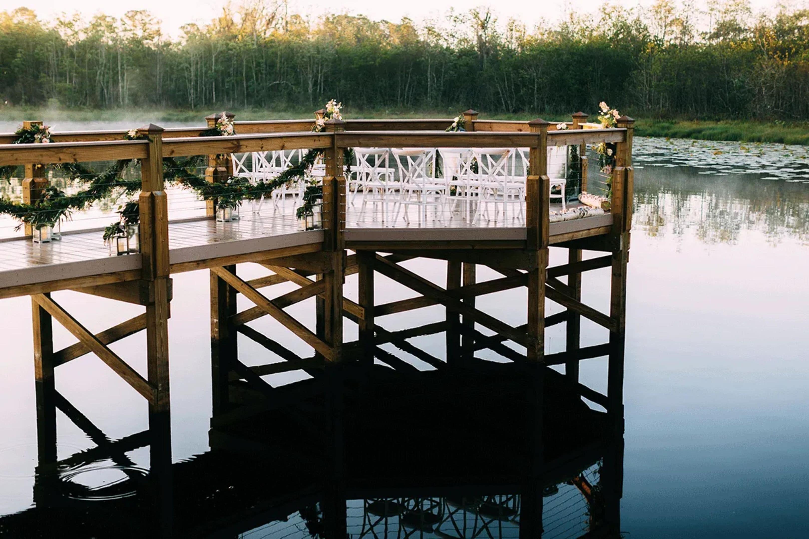 A wooden dock extending over calm water with a forested background.