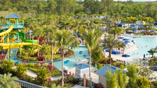 Un resort con una piscina grande, toboganes acuáticos, palmeras y sombrillas de playa.