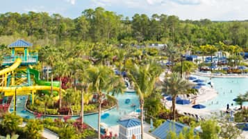 Relax by the large central pool surrounded by lush greenery and palm trees, with a water park and lounge areas nearby.