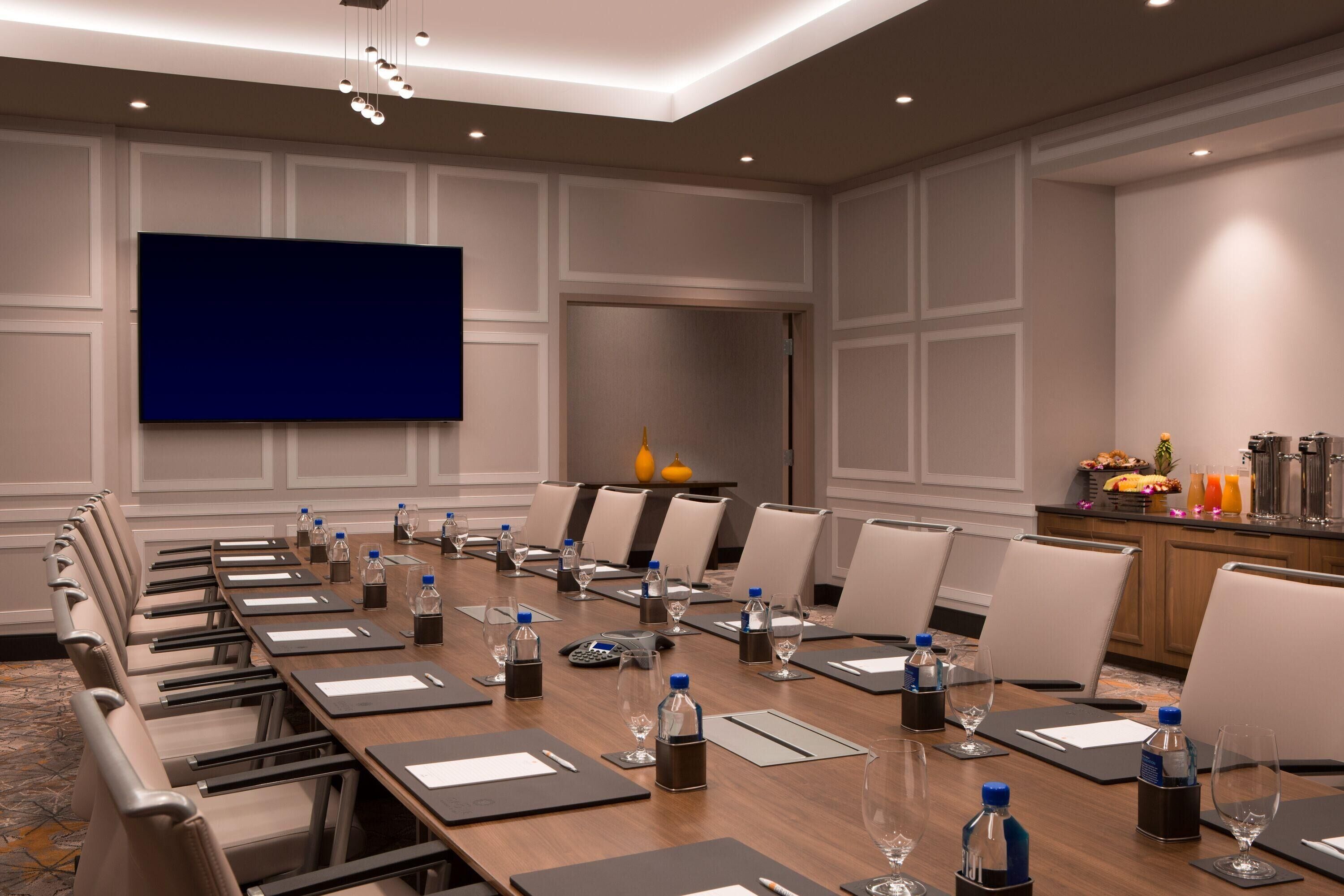 Une salle de conférence équipée d’une longue table, de chaises, d’un grand écran et d’un espace buffet où sont servis des plats et des boissons.