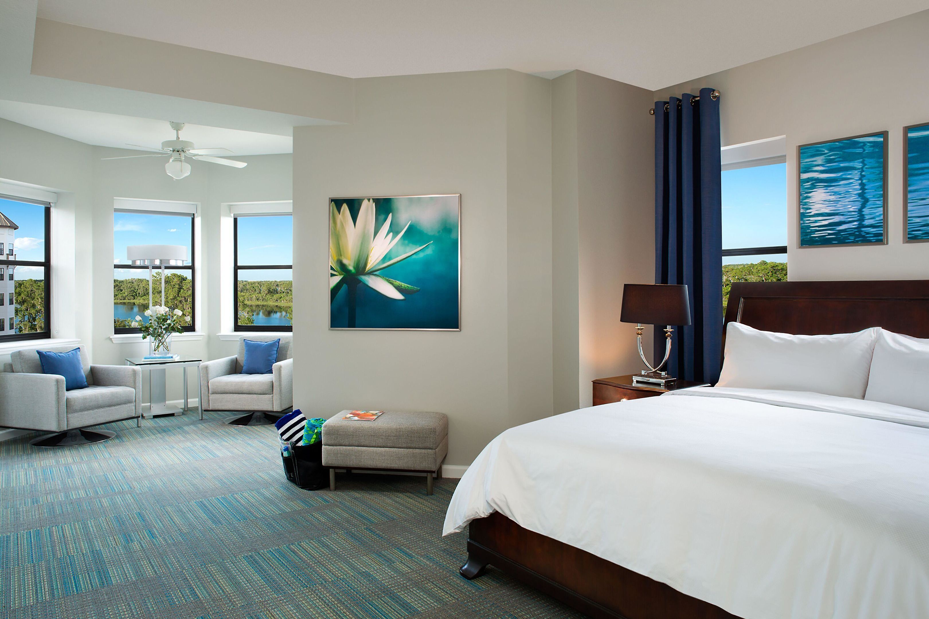 A hotel room with a large bed, two armchairs, a small table, and a view of the outdoors.