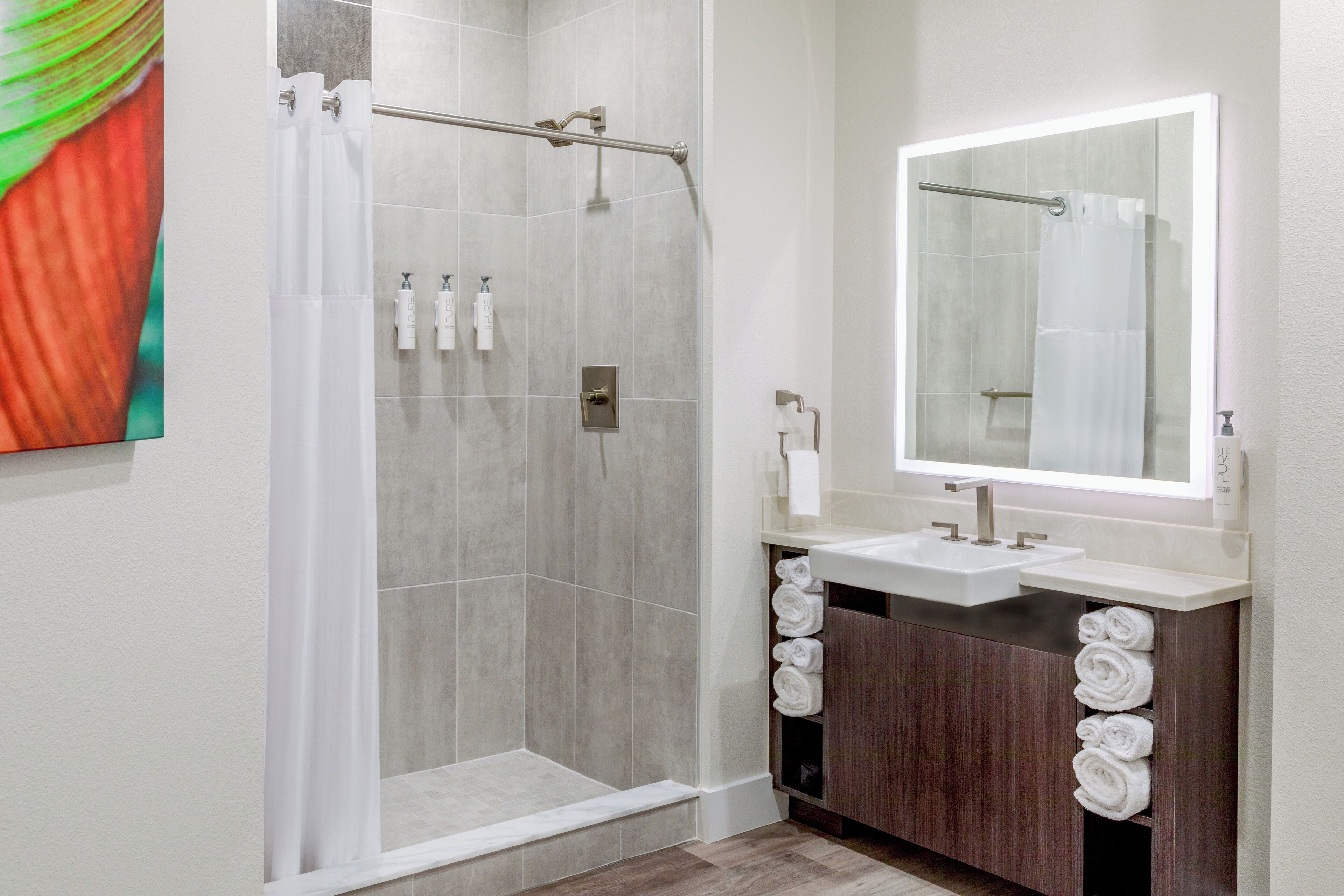 A modern bathroom with a glass shower enclosure, a vanity with a mirror, and neatly rolled towels.