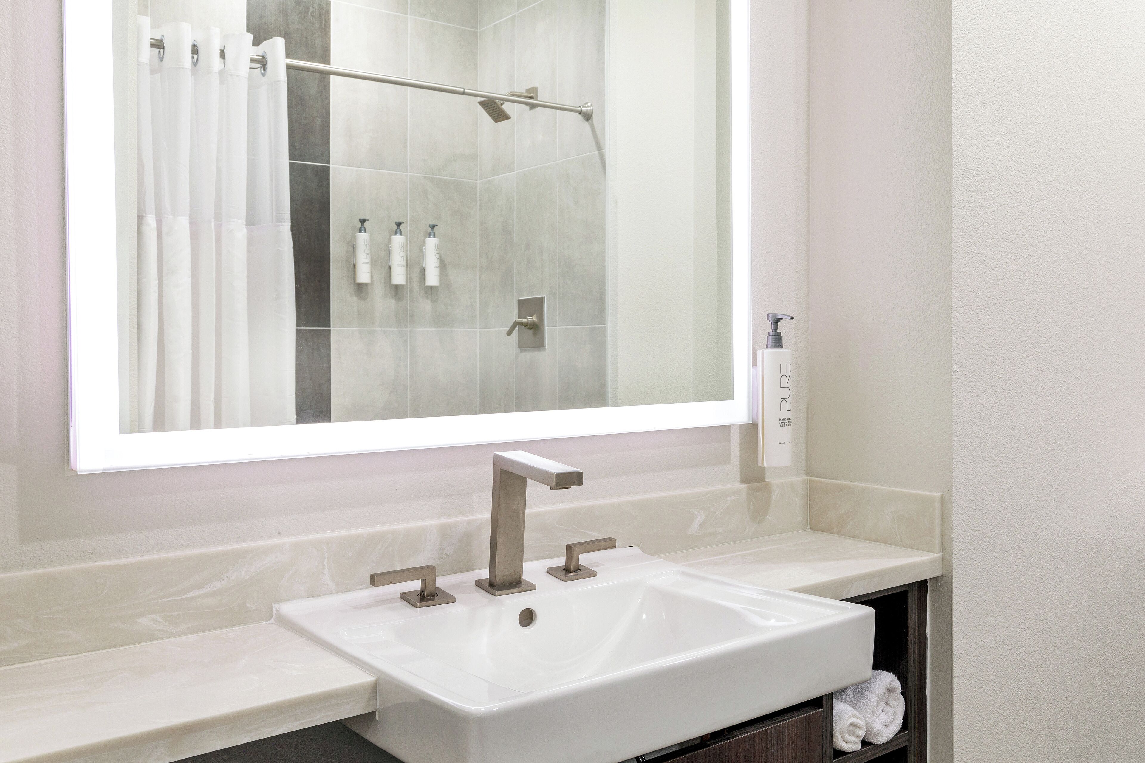 Une salle de bain moderne avec un grand miroir, un lavabo blanc et un espace douche.