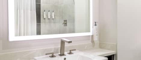 A modern bathroom with a large mirror, a white sink, and a shower area.