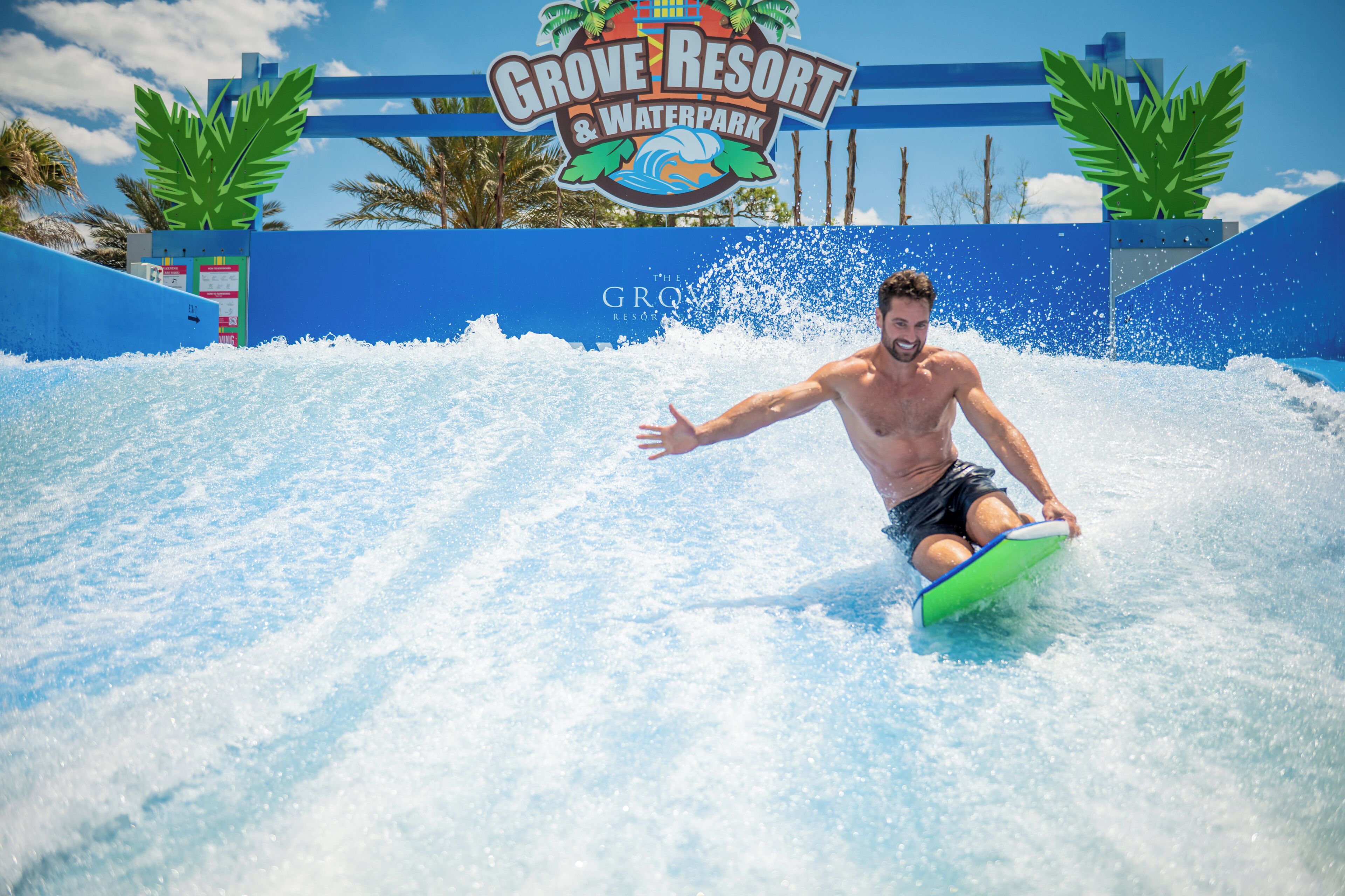 Un hombre surfeando una ola en un parque acuático, con un cartel que dice 'Grove Resort & Waterpark'.