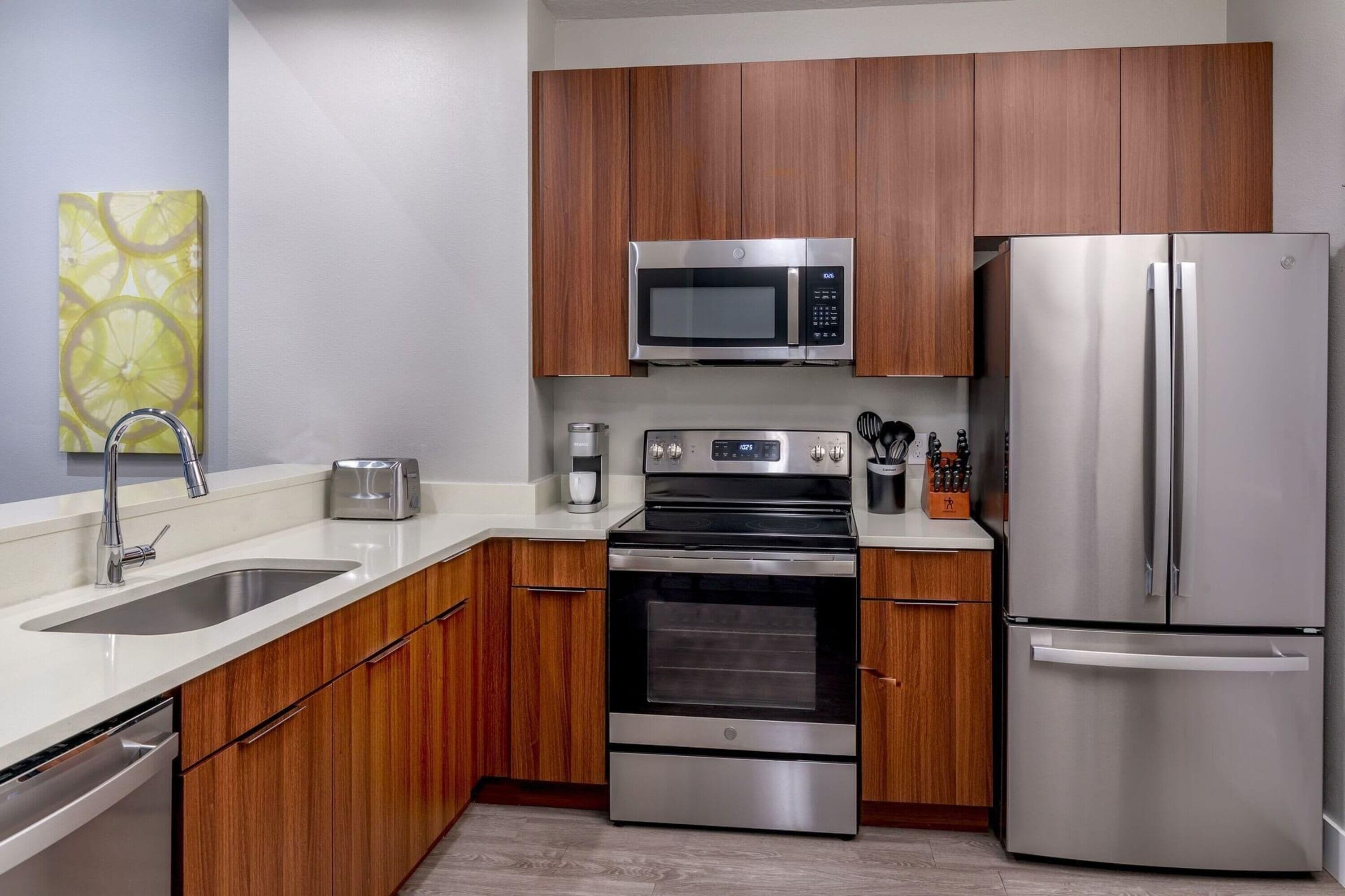 A modern kitchen with stainless steel appliances, wooden cabinets, and a white countertop.