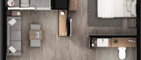 A hotel room with a bed, a desk, a chair, a sofa, a small table, a plant, and a bathroom with a toilet and sink.
