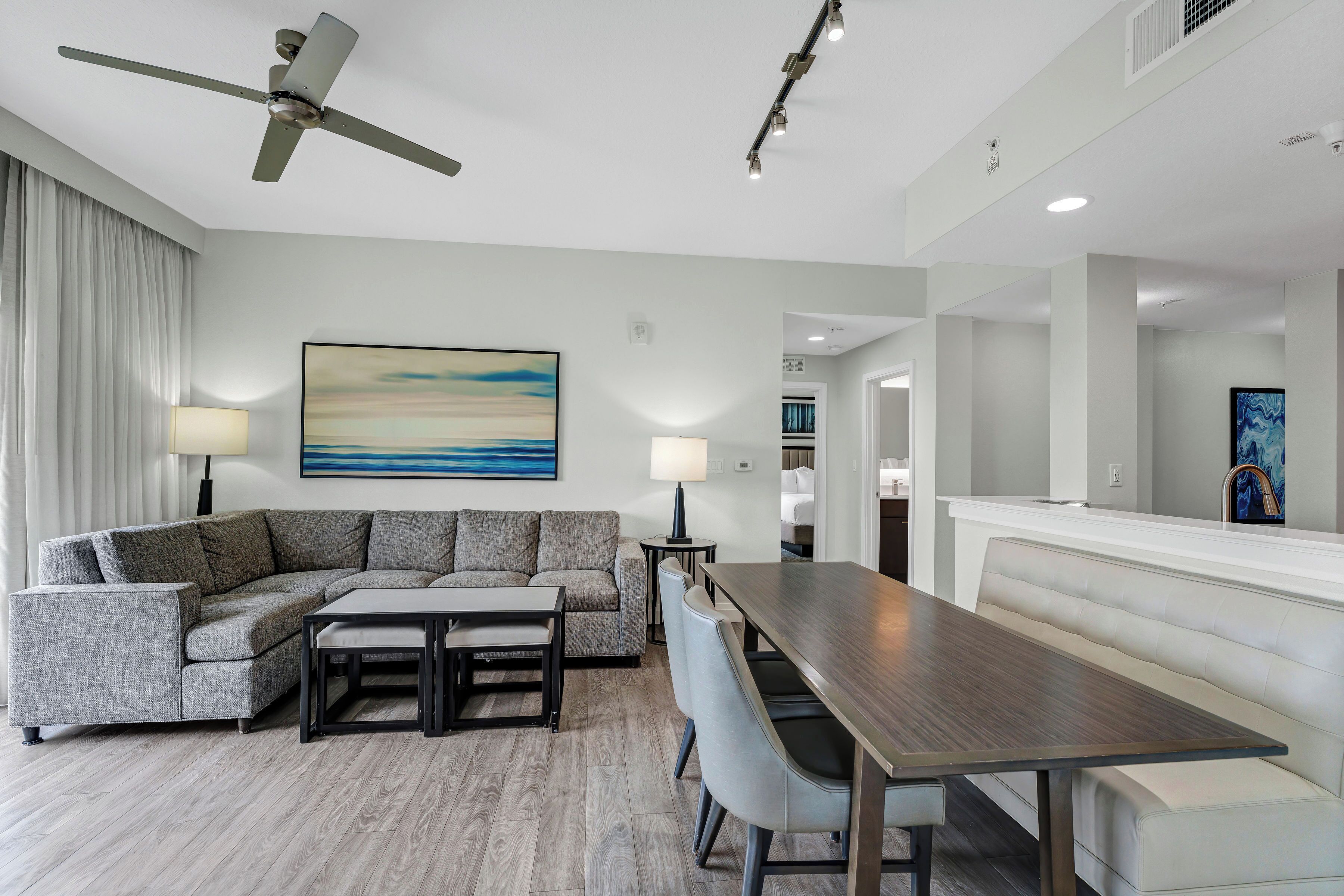 A modern hotel room with a sectional sofa, a dining table, and a ceiling fan.