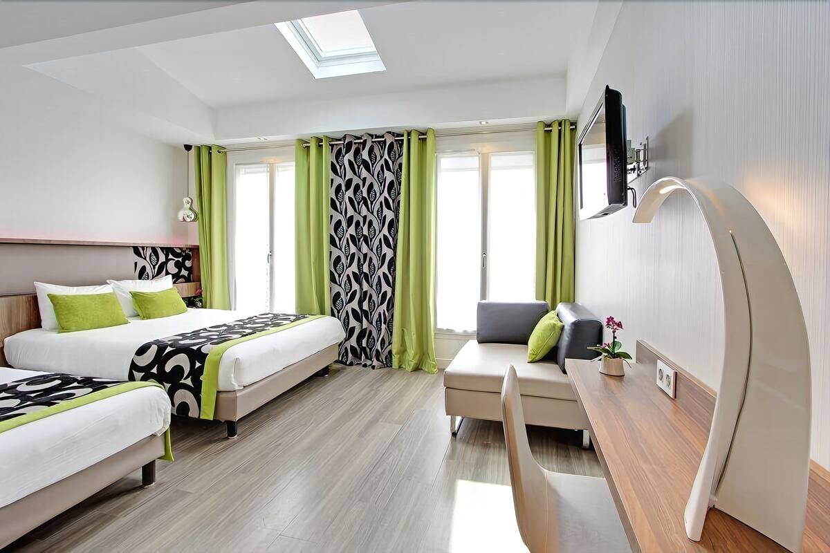 Quarto de hotel com duas camas, uma escrivaninha, uma cadeira, uma televisão e uma janela com cortinas.