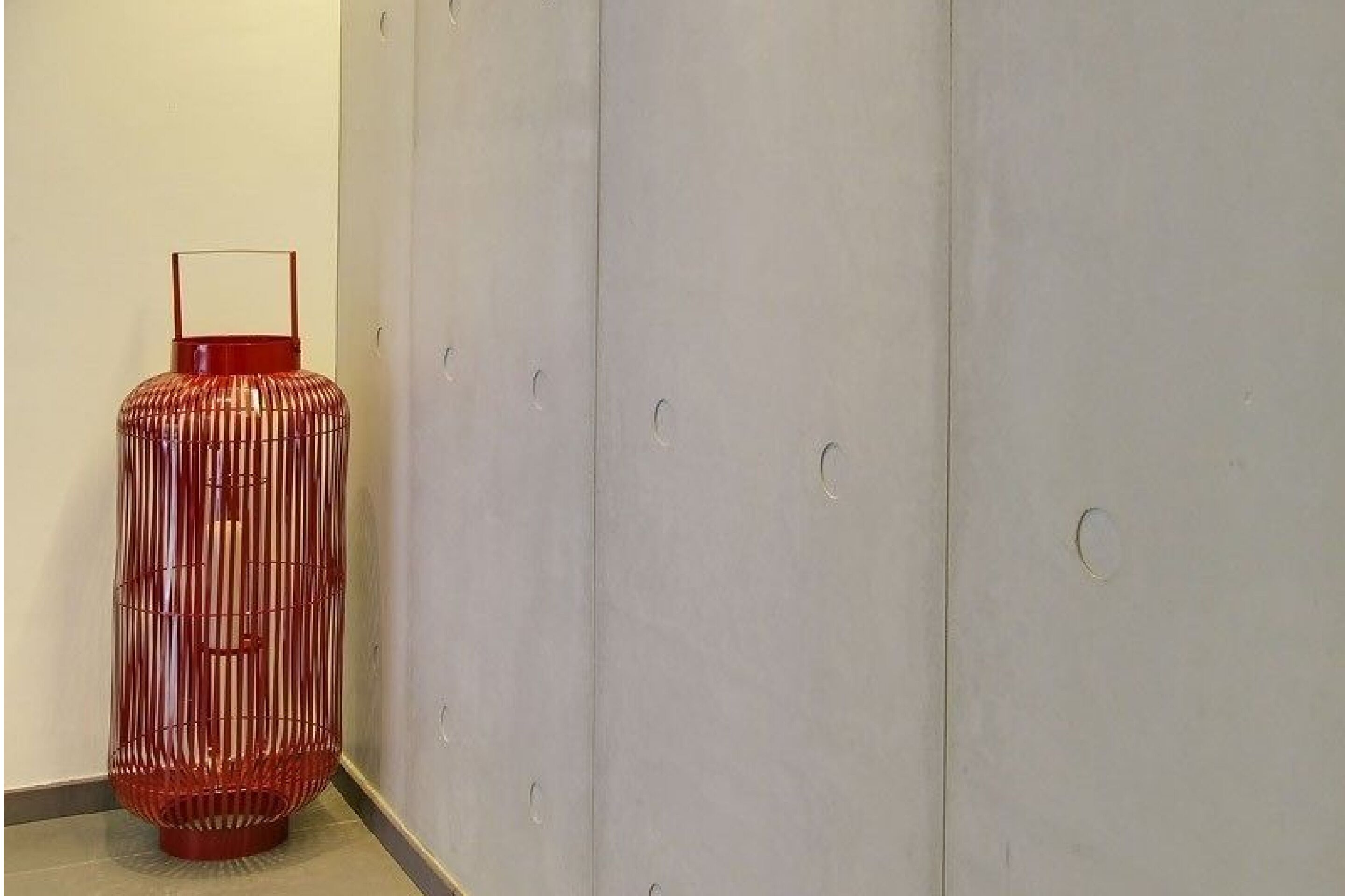 A red cylindrical object with a handle against a plain wall.