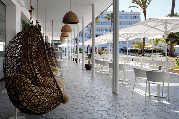 An outdoor seating area with white tables and chairs, a hanging rattan chair, and a white umbrella structure. - AluaSoul Ibiza -Adults Only - Hyatt Inclusive Collection (Santa Eulalia del Rio)