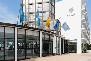 Un edificio moderno con varias banderas, incluyendo azul y amarillo, y el nombre 'ALUASOUL' en la fachada.