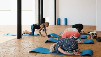 A group of people practicing yoga on blue mats in a room with a tiled floor and large windows.