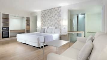 Habitación de hotel moderna con cama, sofá, una mesita, una caja fuerte empotrada y un baño visible a través de una puerta abierta.