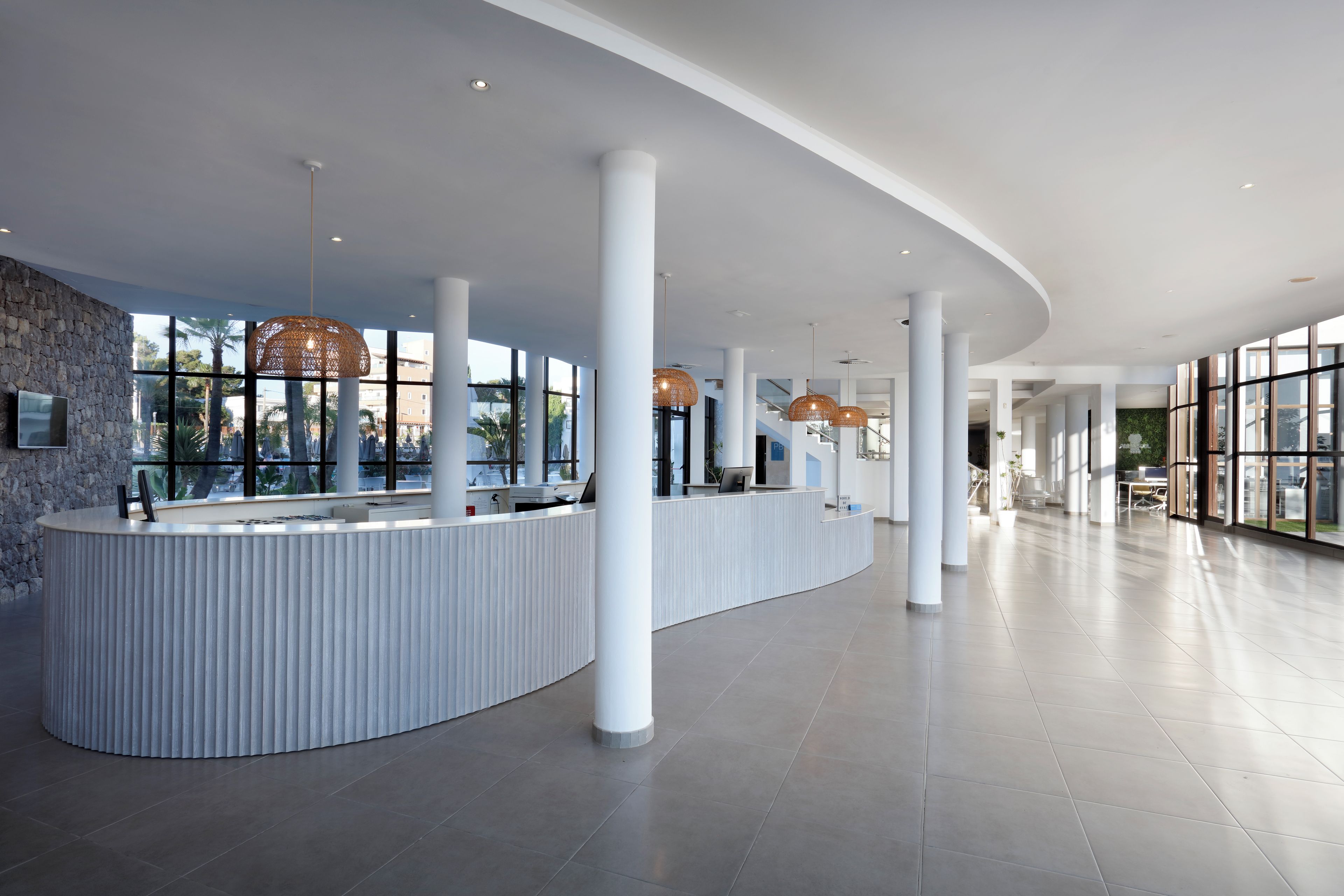 A modern reception area with a curved white reception desk, large windows, and hanging rattan pendant lights.