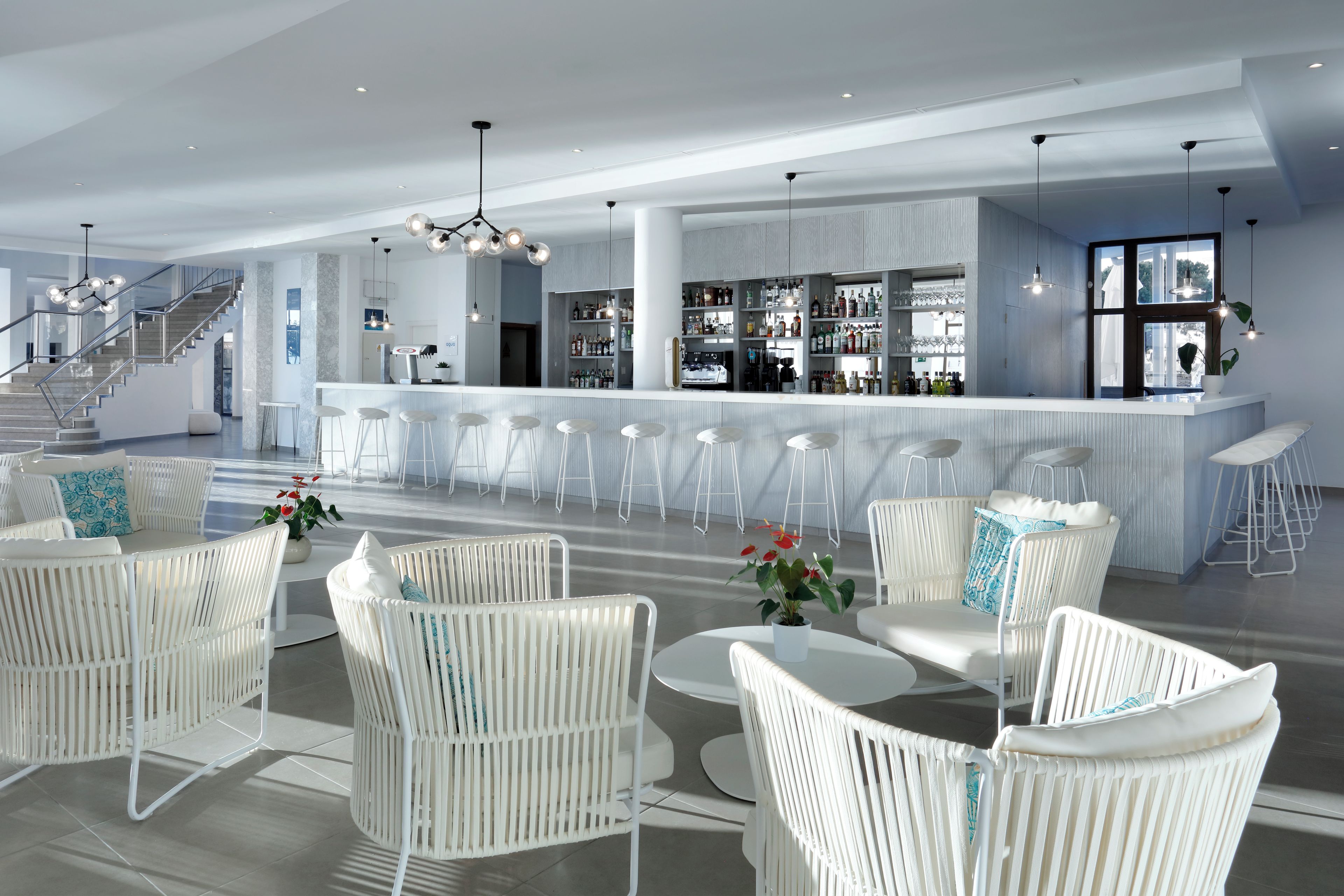 A modern bar area with white bar stools, a bar counter, and a staircase leading to an upper level.