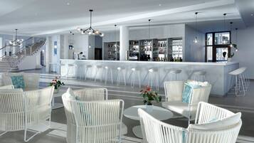 A modern bar area with white bar stools, a bar counter, and a staircase leading to an upper level.