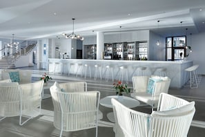Uma área de bar moderna com banquetas brancas, balcão e escada para um andar superior.