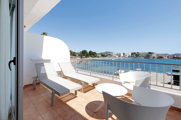 Un balcon avec vue sur une plage et la mer. On y trouve des chaises longues et une petite table.