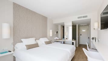 A hotel room with two beds, a desk, a chair, a TV, and a bathroom visible through an open door.