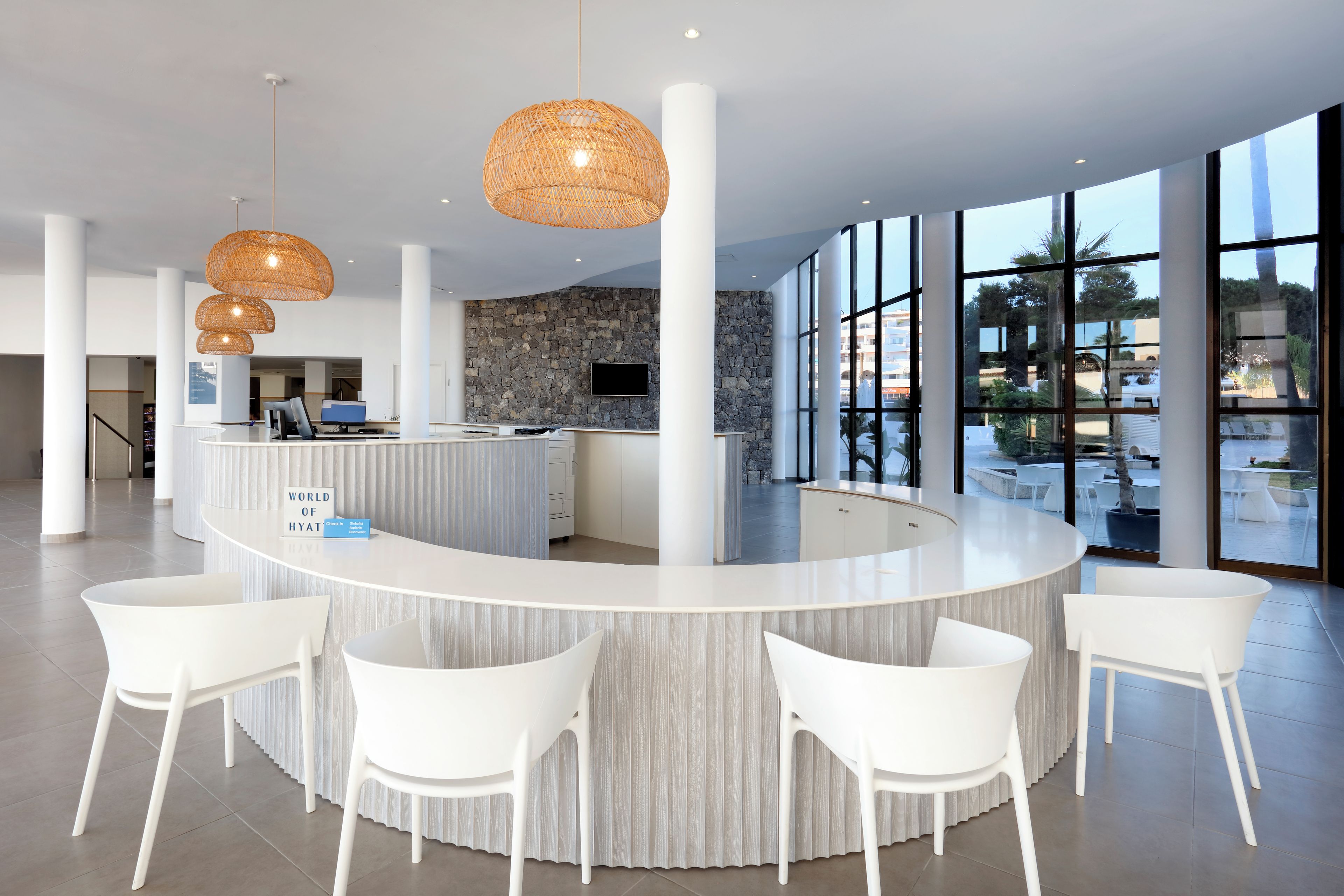 Een moderne hotellobby met een gebogen receptiebalie, witte stoelen en grote ramen met uitzicht op het groen.