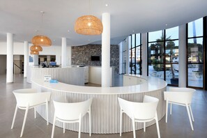 A modern hotel lobby with a curved reception desk, white chairs, and large windows offering views of the outdoors. - AluaSoul Ibiza -Adults Only - Hyatt Inclusive Collection (Santa Eulalia del Rio)