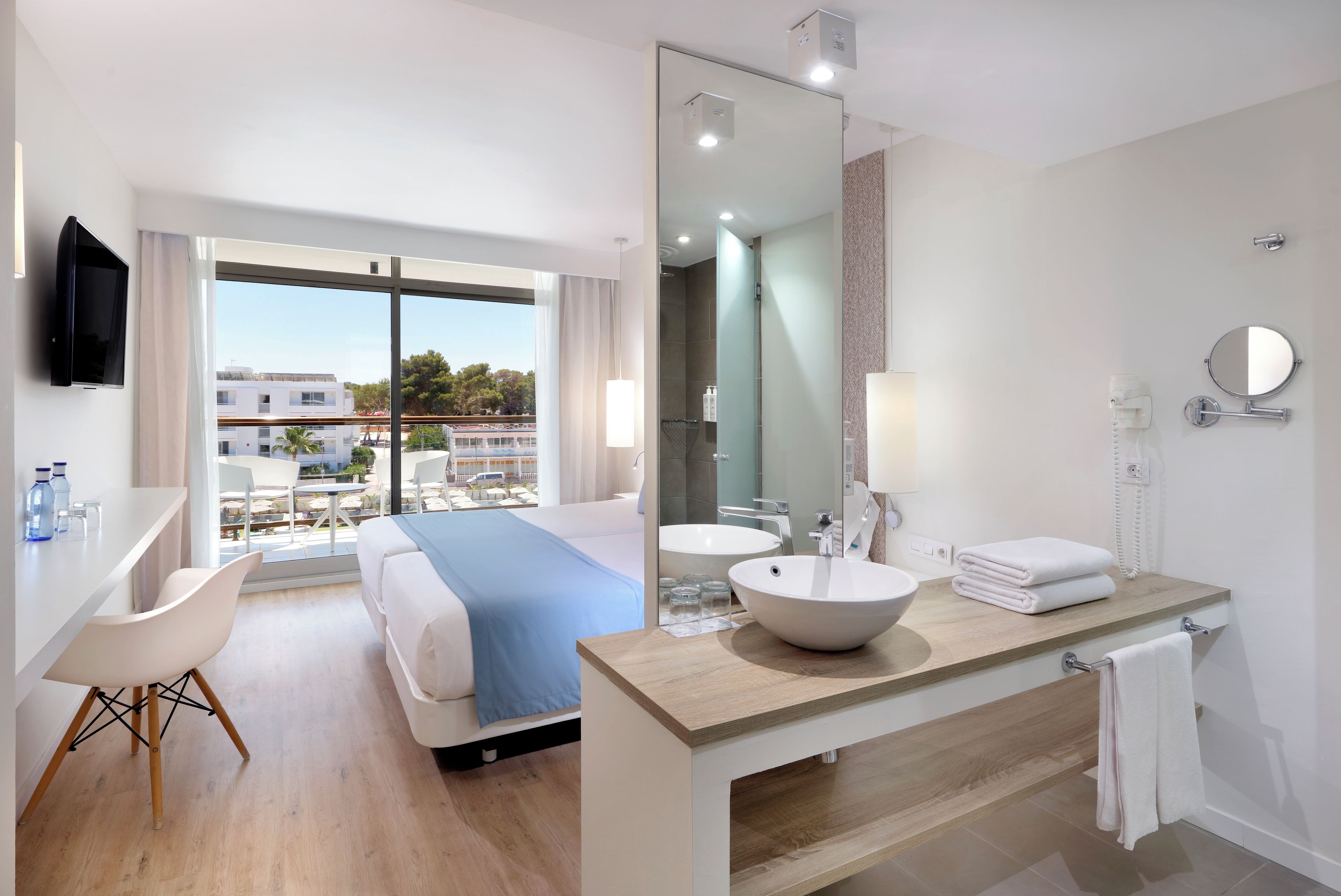 Una camera d'albergo con un letto, una scrivania, un bagno con lavandino e specchio, e vista sulla città.