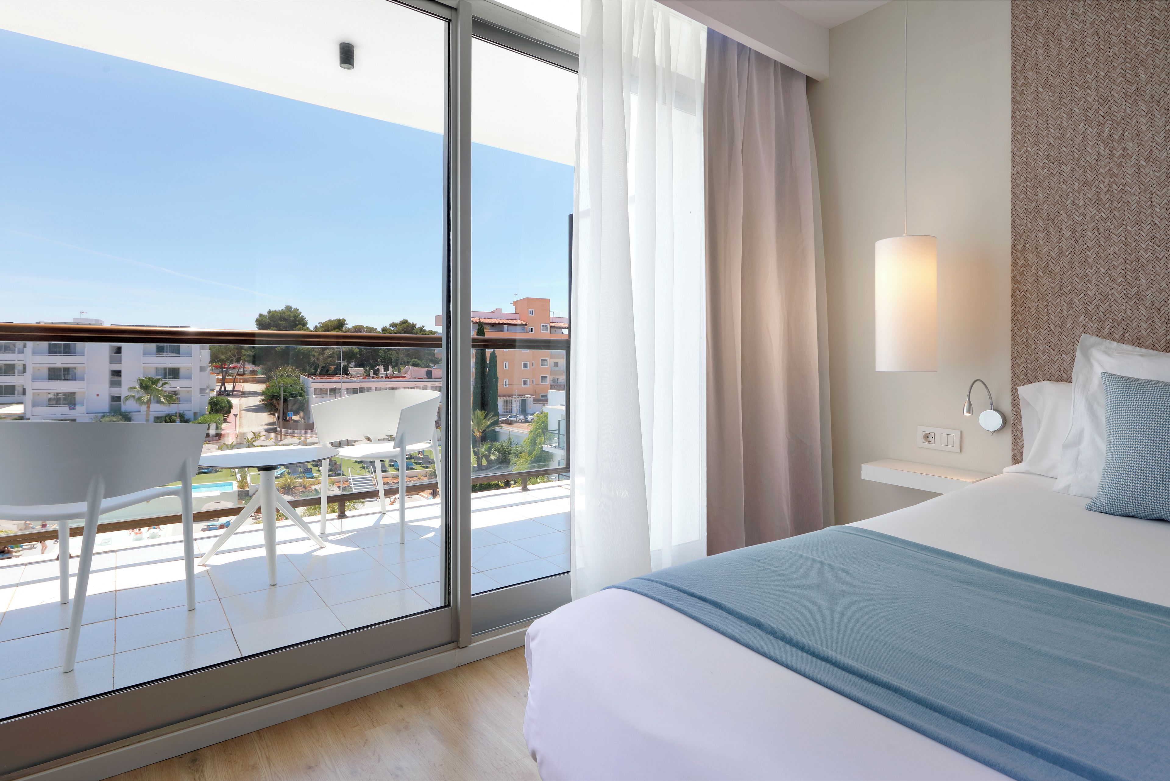 Una habitación de hotel con balcón, cama, mesita de noche y vista a la ciudad.