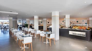 A modern dining area with tables and chairs, a buffet with various food items, and a view of the outdoors.