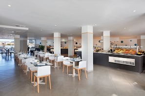 Un'area ristorazione moderna con tavoli e sedie, un buffet con diversi piatti e vista sull'esterno.