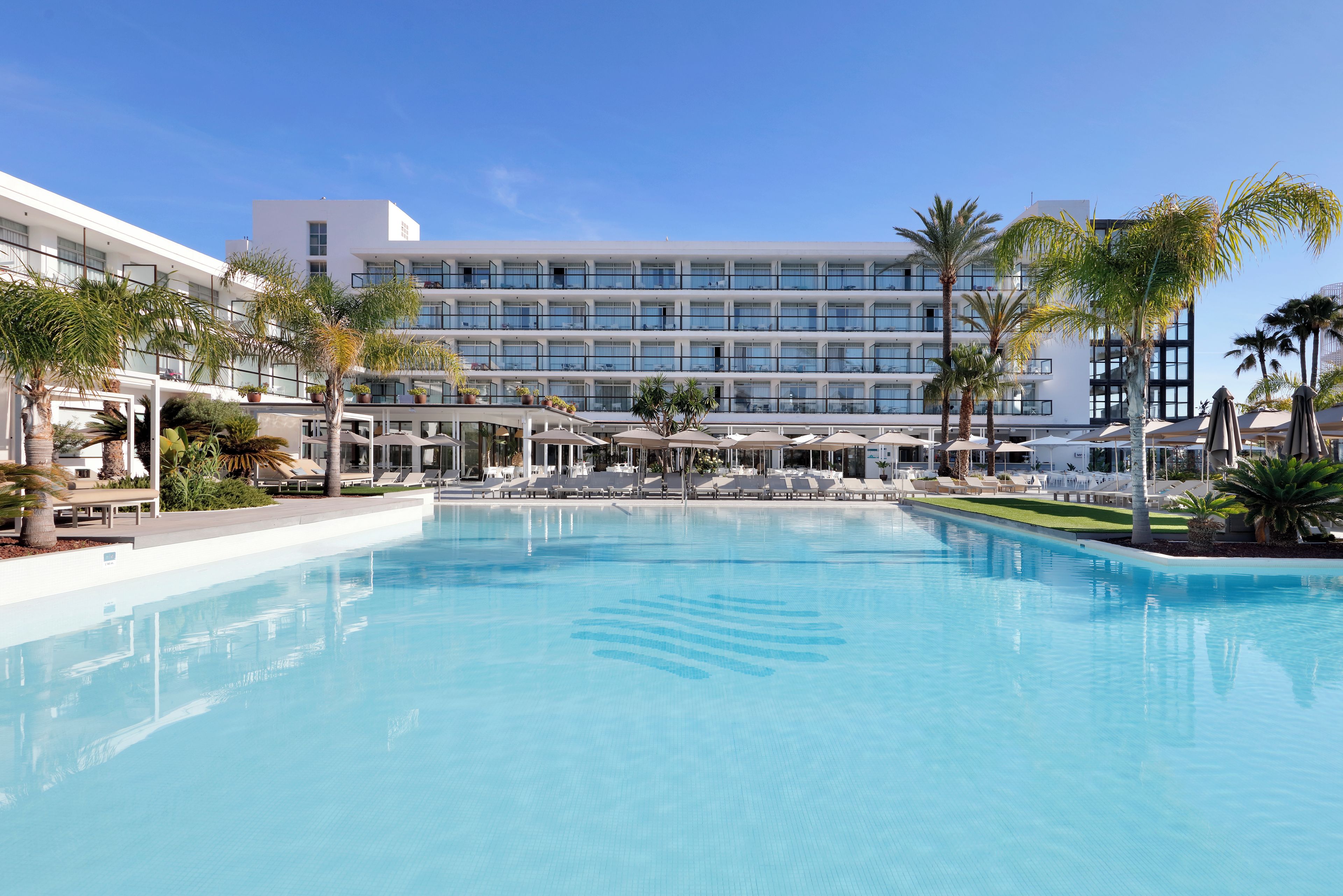 A hotel with a large swimming pool, multiple balconies, and palm trees.