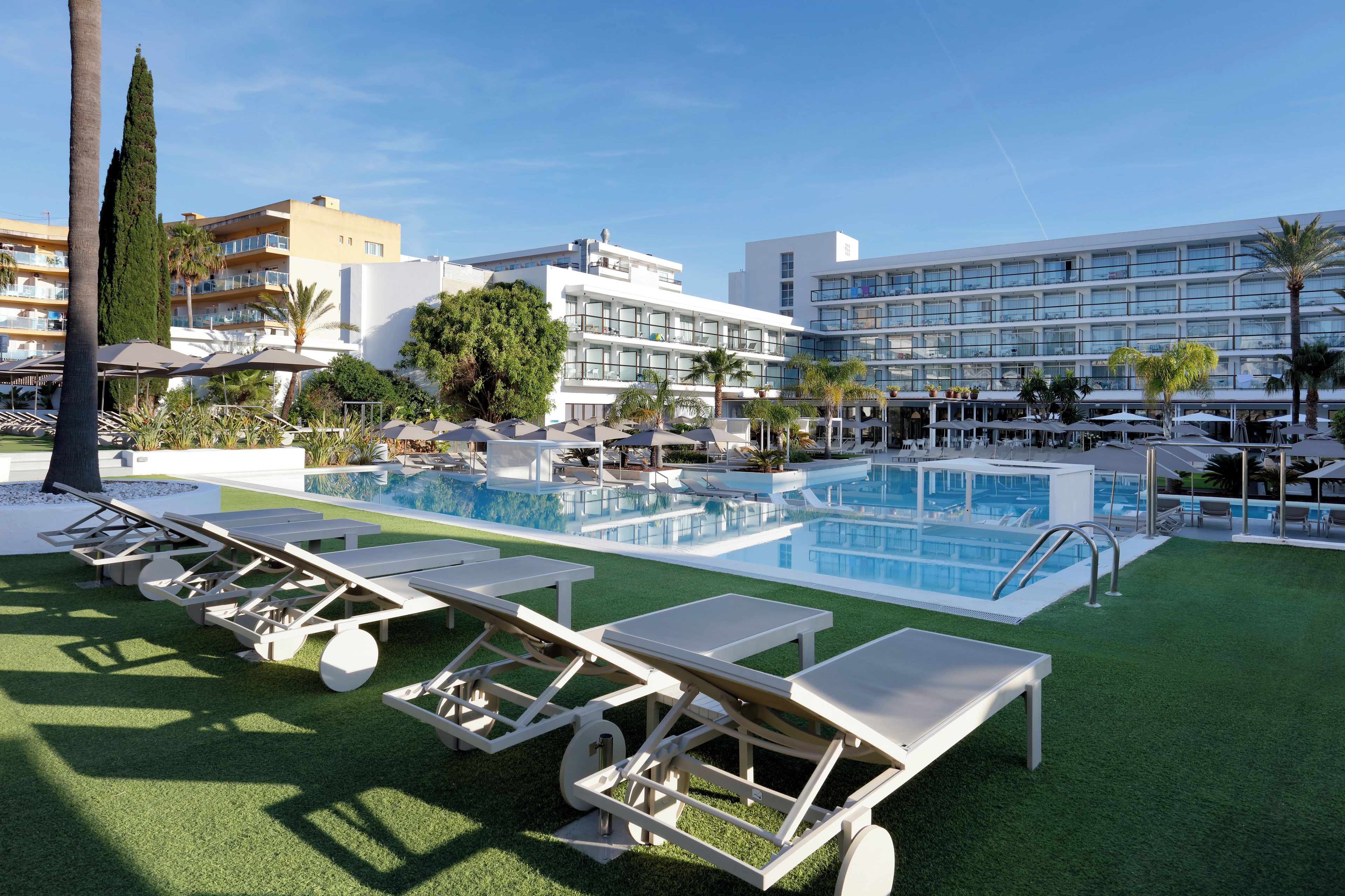 Zona de piscina con tumbonas y un edificio grande al fondo.