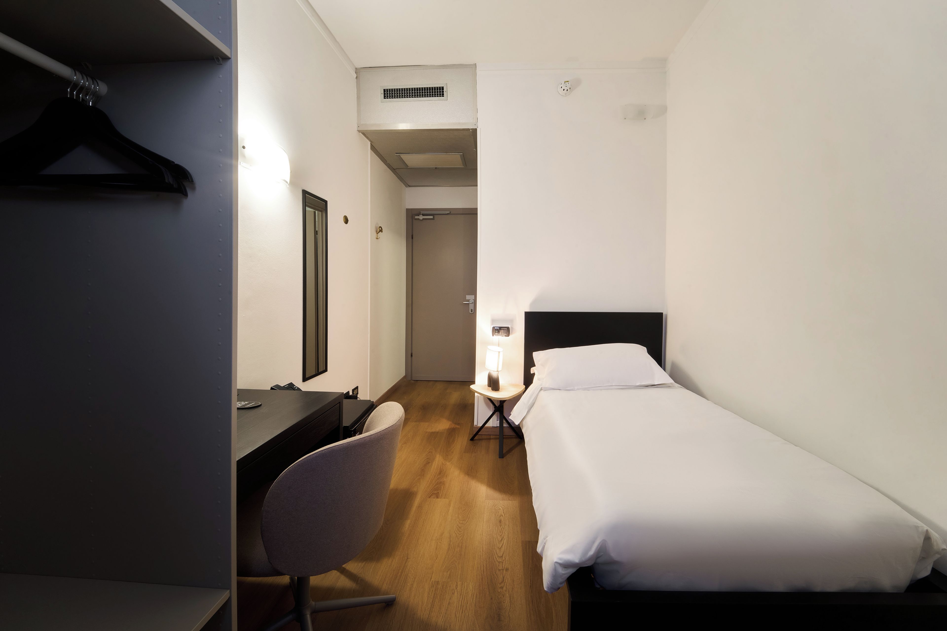 Una habitación de hotel con una cama, un escritorio, una silla y un armario.