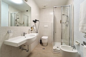 Een moderne badkamer met een grote spiegel, twee wastafels, een toilet en een douche met glazen wanden.