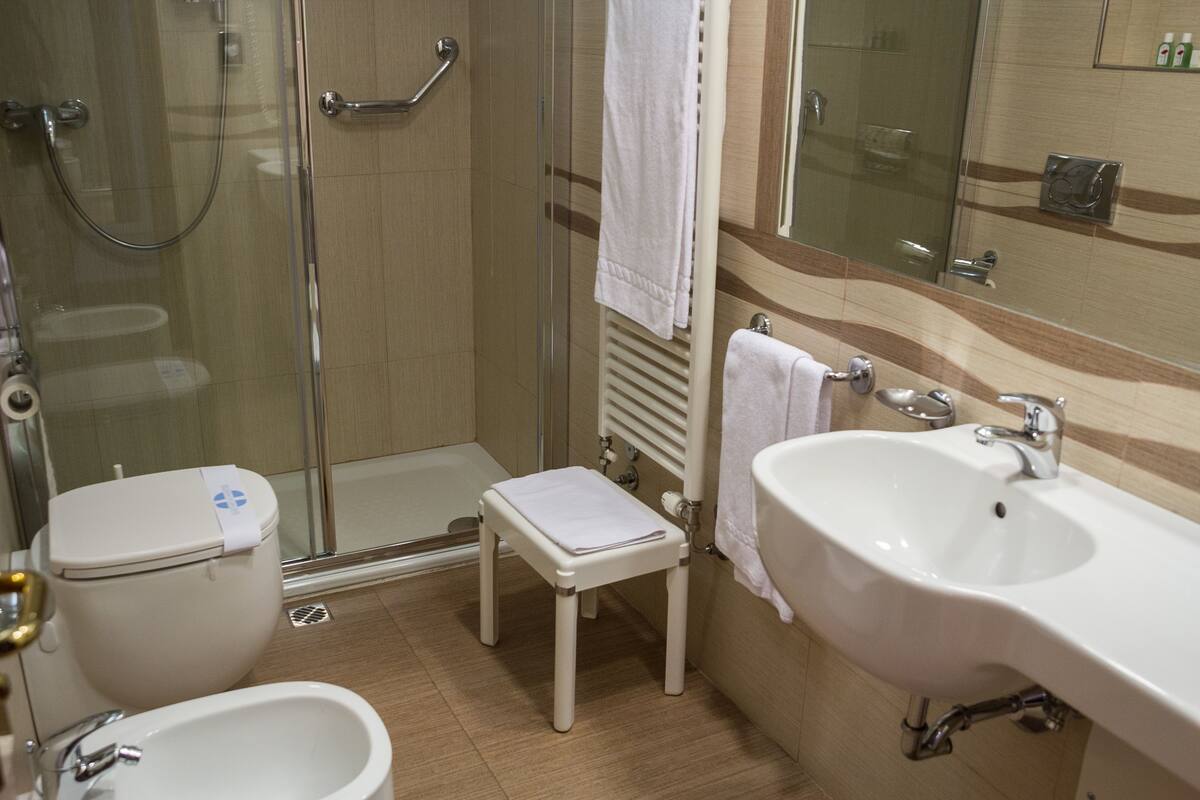 Une salle de bain avec une douche à parois de verre, un lavabo blanc et un petit tabouret blanc.
