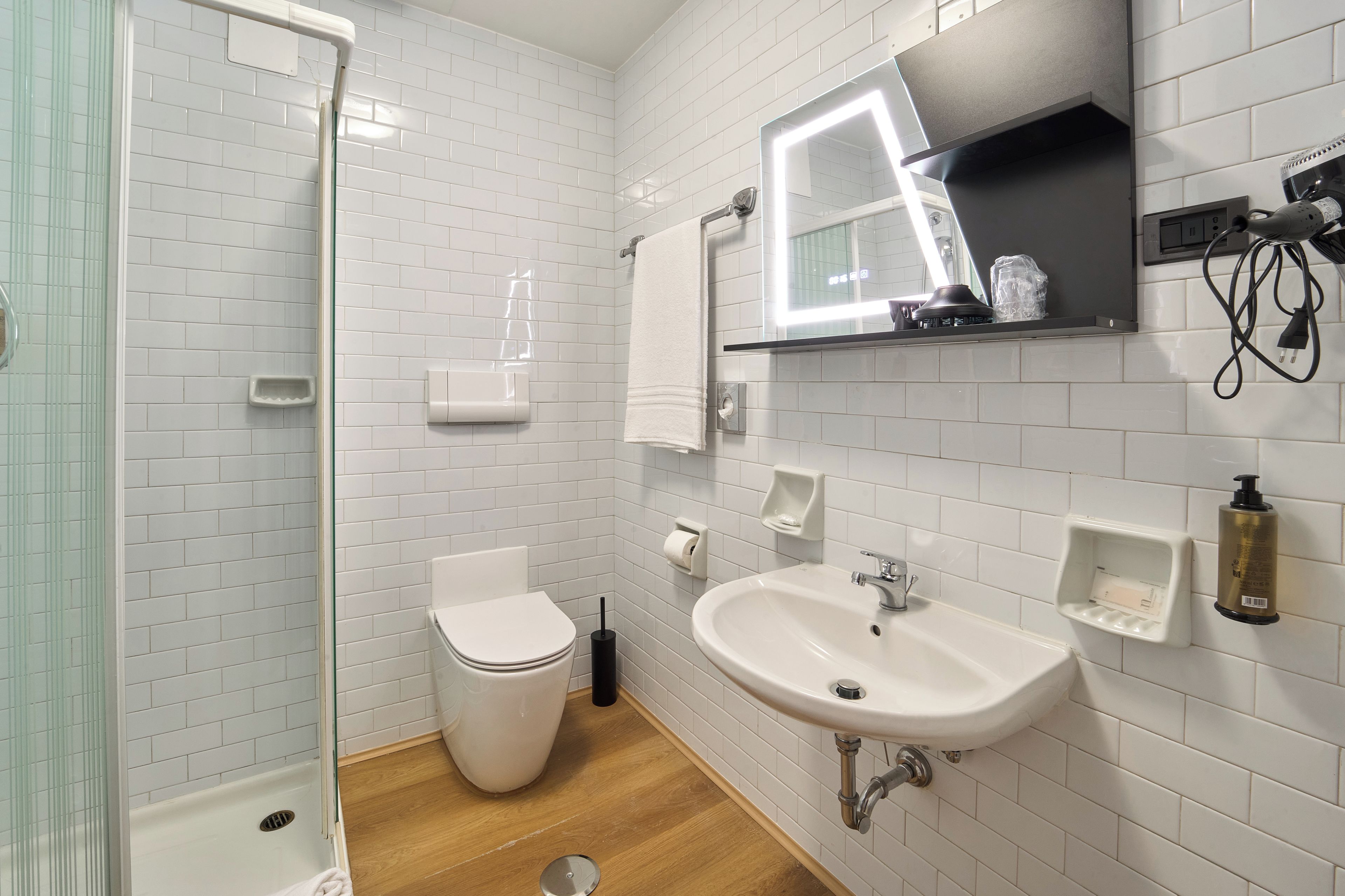 A modern bathroom with white subway tiles, a white toilet, a sink with a mirror above it, and a shower area.