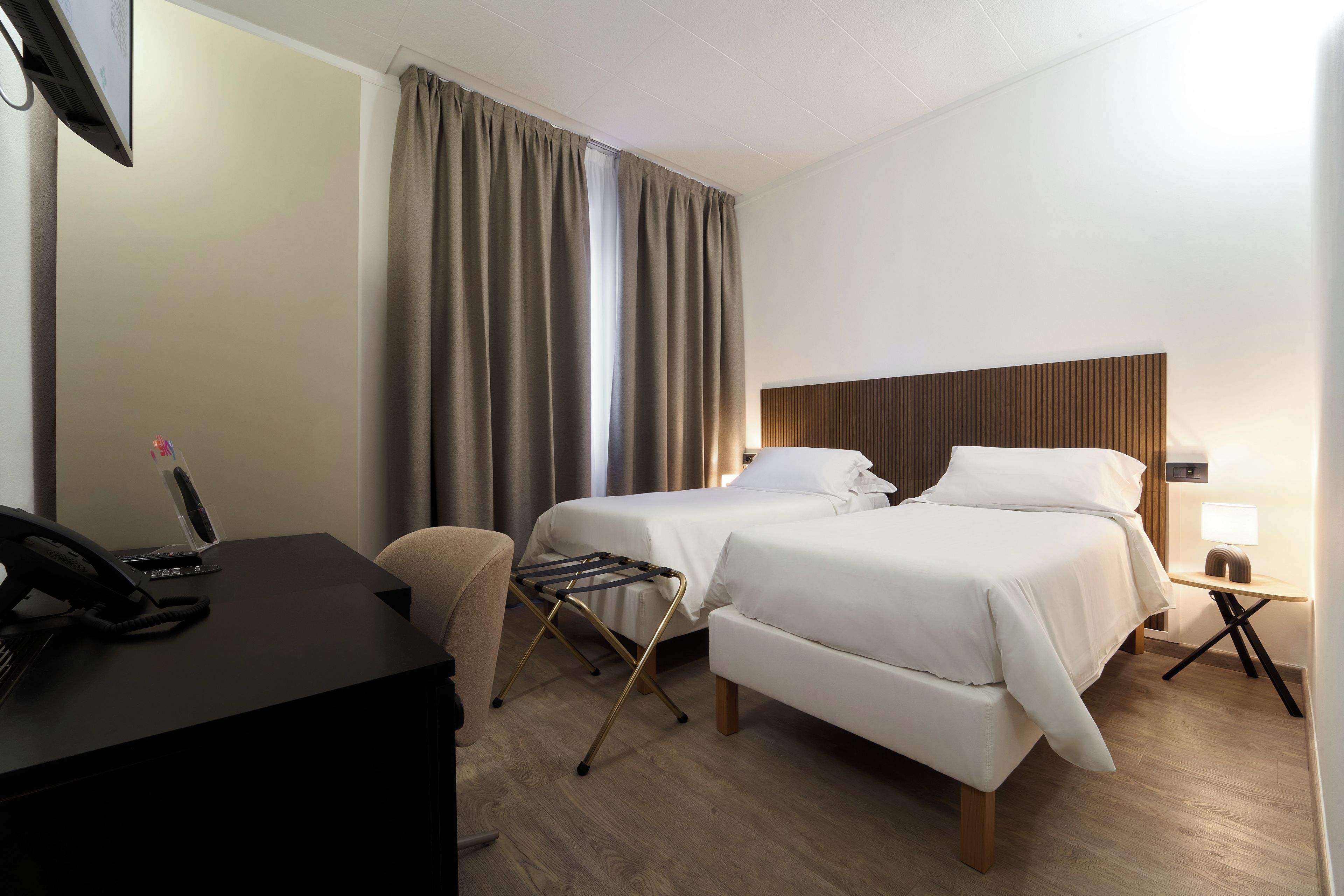 A hotel room with two beds, a desk, a telephone, and a lamp.