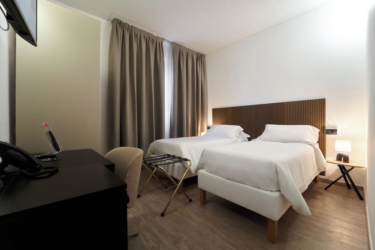 Een hotelkamer met twee bedden, een bureau, een telefoon en een lamp.