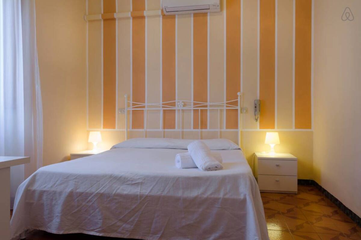 Habitación de hotel con una cama, dos mesitas de noche con lámparas, aire acondicionado en la pared y un diseño de pared a rayas.