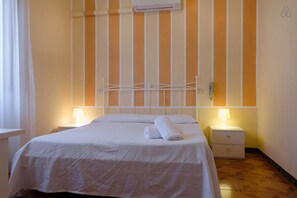 Quarto de hotel com uma cama, duas mesas de cabeceira com abajures, ar condicionado fixado na parede e um design de parede listrado.
