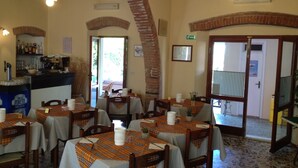 A restaurant with multiple tables, each covered with a plaid tablecloth. There are brick arches and wooden beams on the ceiling. A bar area with bottles and glasses is visible in the background.