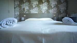 A neatly made bed with white linens and two rolled towels on either side.