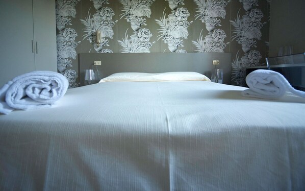 A neatly made bed with white linens and two rolled towels on either side.