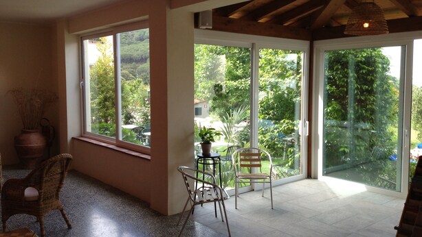 A spacious room with large windows, a dining area with chairs, a table, and a potted plant.