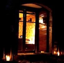 Un arco de entrada da a un espacio interior cálidamente iluminado, con una pared de piedra y un estante con objetos.