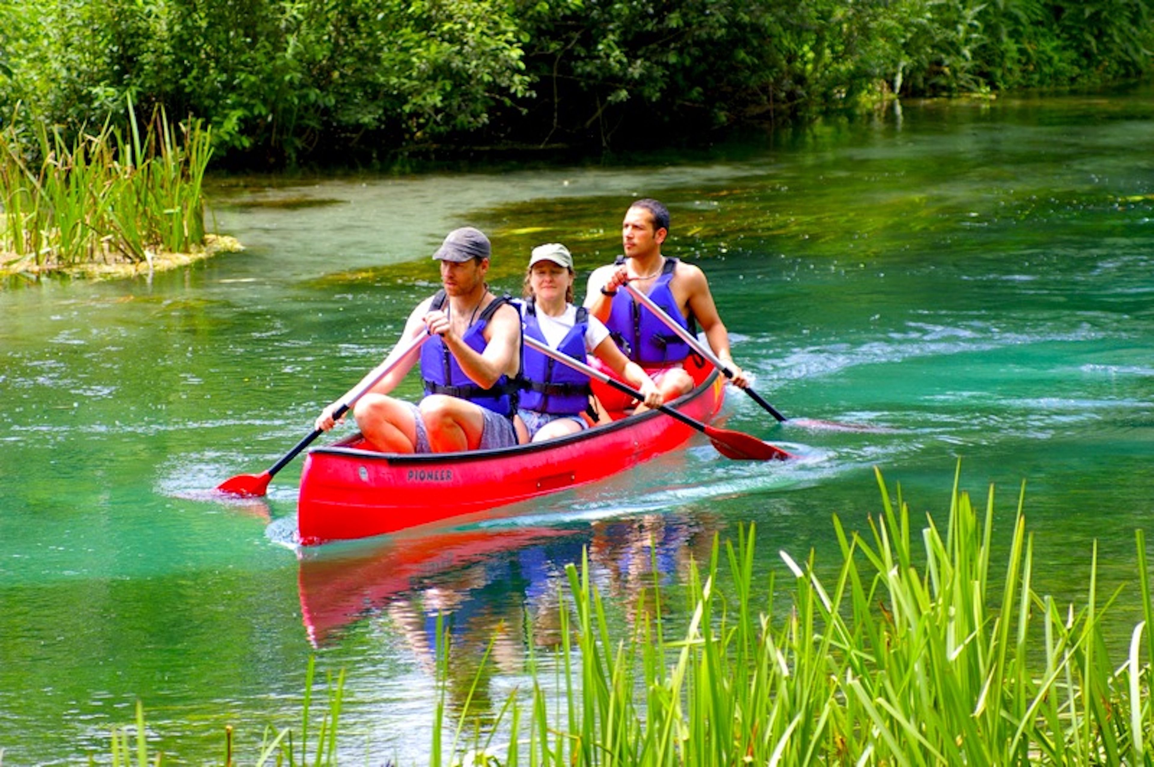 Three people in a red canoe on a river surrounded by greenery.