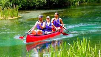 Three people in a red canoe on a river surrounded by greenery.